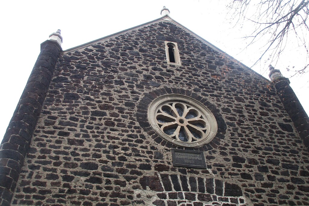 Der obere Bereich der Fassade der Synagoge in der Ostergasse in Polch mit dem Tuffsteinradfenster und darüber dem schlitzartigen maurischen Fenster (2022).