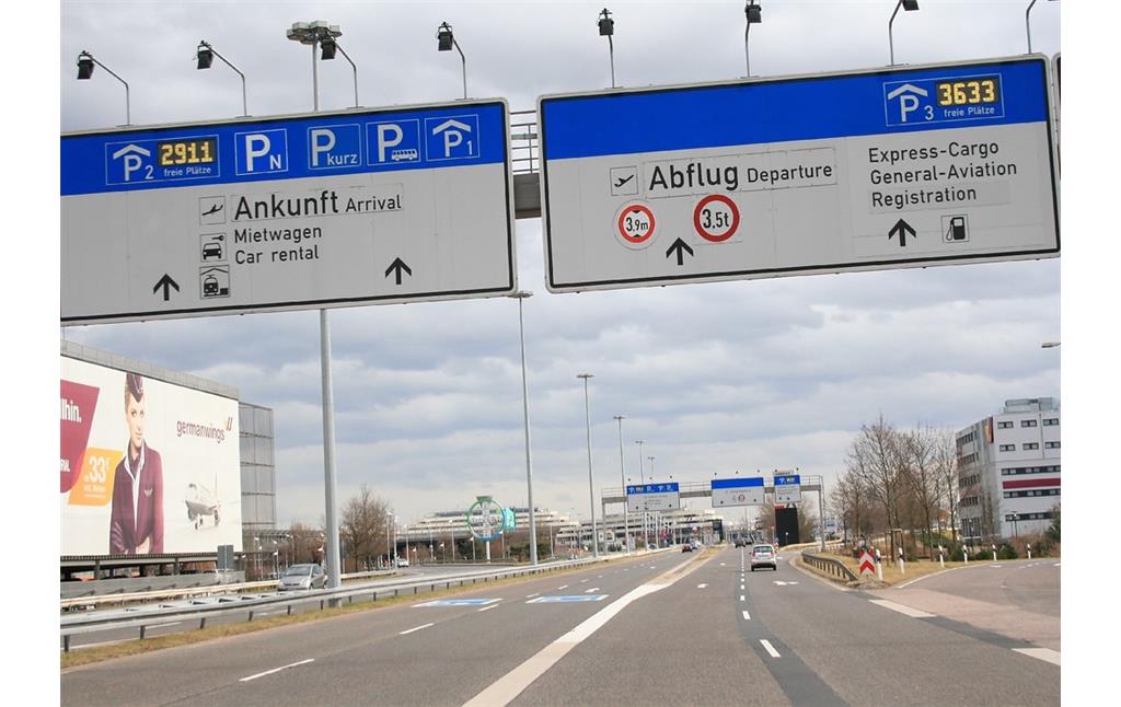 Anfahrt auf der Kennedystraße (L 84) zum Flughafen Köln/Bonn (2015), links der Straße das vor Ort befindliche Bayer-Kreuz.