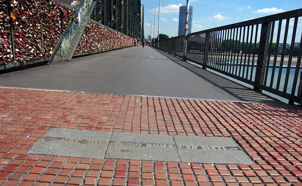 In das Pflaster eingelassene metallene Gedenkinschrift, die an die Deportation von Roma und Sinti über die Gleise von "Deutz-Tief" am Bahnhof Köln Messe/Deutz im Mai 1940 erinnert, am südwestlichen Zugang zur Hohenzollernbrücke (2015).