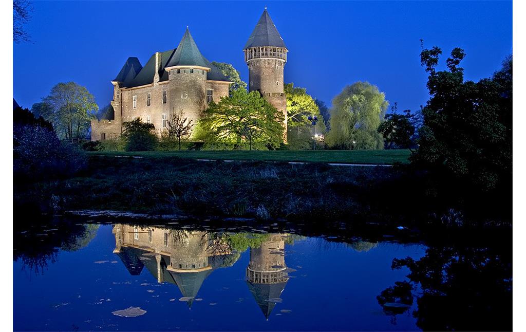 Die auf das 12. Jahrhundert zurückgehende Wasserburg Linn bei Krefeld bei Nacht; das Bauwerk spiegelt sich im bewässerten Burggraben (2005)