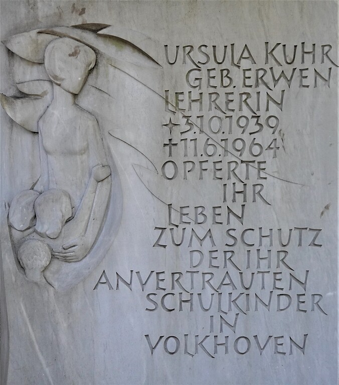 Die Inschrift und das Schutzmantel-Ornament auf dem Grabstein der Lehrerin Ursula Kuhr, Opfer des Attentats von Köln-Volkhoven, auf dem Kölner Südfriedhof (2023).