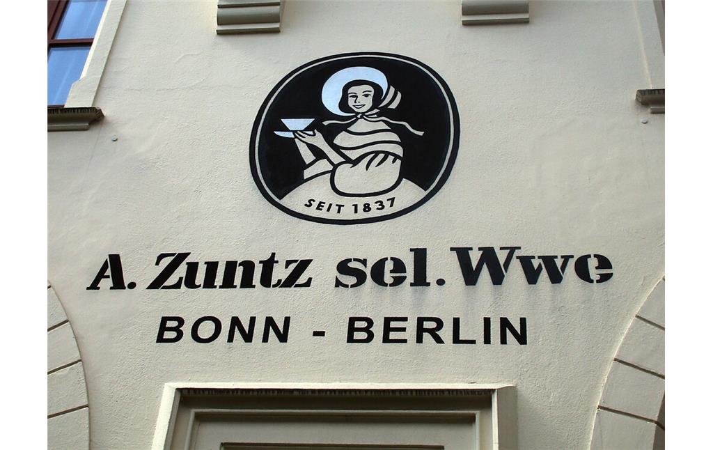 Das Firmenlogo der "Dame mit dem Schutenhut" an der erhaltenen Fassade der einstigen Kaffeerösterei Zuntz ("A. Zuntz sel. Wwe.") in der Königstraße in der Bonner Südstadt (2022). Unter dem Logo befindet sich die Inschrift "A. Zuntz sel. Wwe / Bonn - Berlin".
