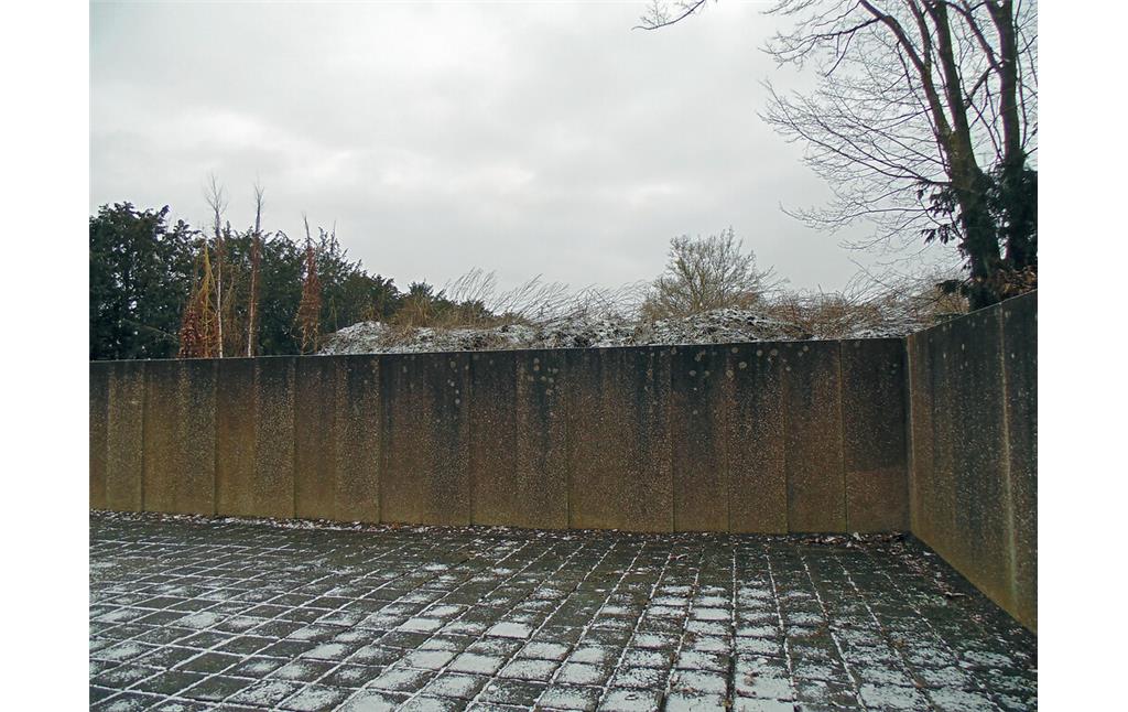 Blick auf den Komposthaufen hinter dem Eingangsbereich des Gräberfelds für deutsche und ausländische Opfer des Nationalsozialismus auf dem Westfriedhof in Köln-Vogelsang (2021).