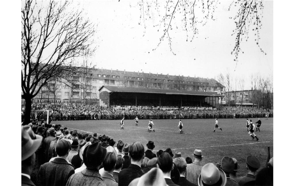 Blick über den Fußballplatz auf die Tribüne des Stadions Köln-Weidenpesch bei einem Spiel des VfL Köln 99 gegen Essen in den 1950er Jahren.