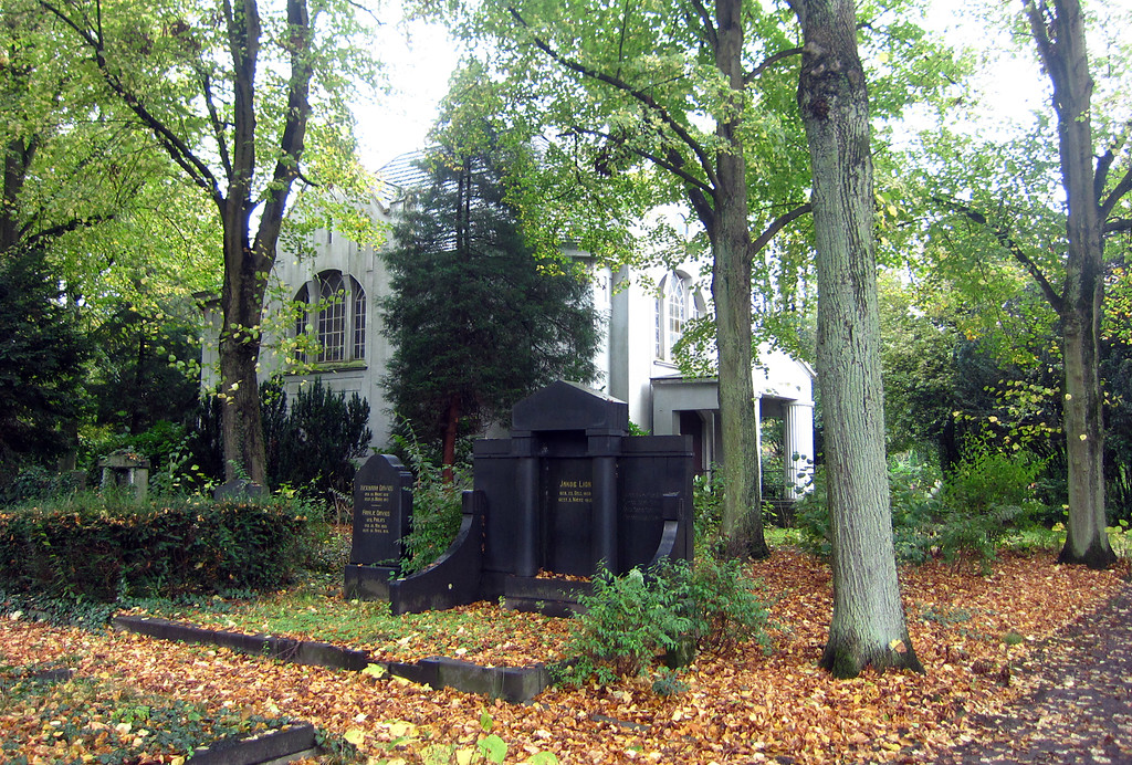Grabmale auf dem baumbestandenen neuen jüdischen Friedhof (Alte Gladbacher Straße) in Krefeld. Im Hintergrund ist die große Trauerhalle zu erkennen (2014).