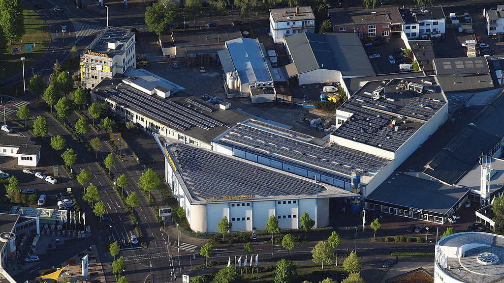 Luftbild-Aufnahme des Betriebsgeländes der Verpoorten GmbH & Co. KG am Potsdamer Platz in Bonn, Ansicht von Süden (2014). Auf den Dachflächen der Gebäude sind zahlreiche Solarzellen der insgesamt 3.500 Quadratmeter großen Photovoltaik-Anlage zu sehen.