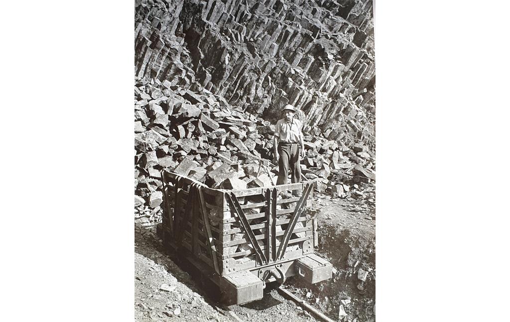 Blick auf einen Arbeiter und eine beladene Lore, dahinter eine Basaltsäulenwand im Dattenberger Steinbruch (1940er Jahre).