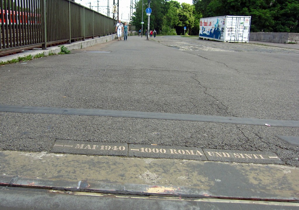 An der südöstlichen Auffahrt zur Hohenzollernbrücke in das Pflaster eingelassene metallene Gedenkinschrift, die an die Deportation von Roma und Sinti über die Gleise von "Deutz-Tief" am Bahnhof Köln Messe/Deutz im Mai 1940 erinnert (2015).