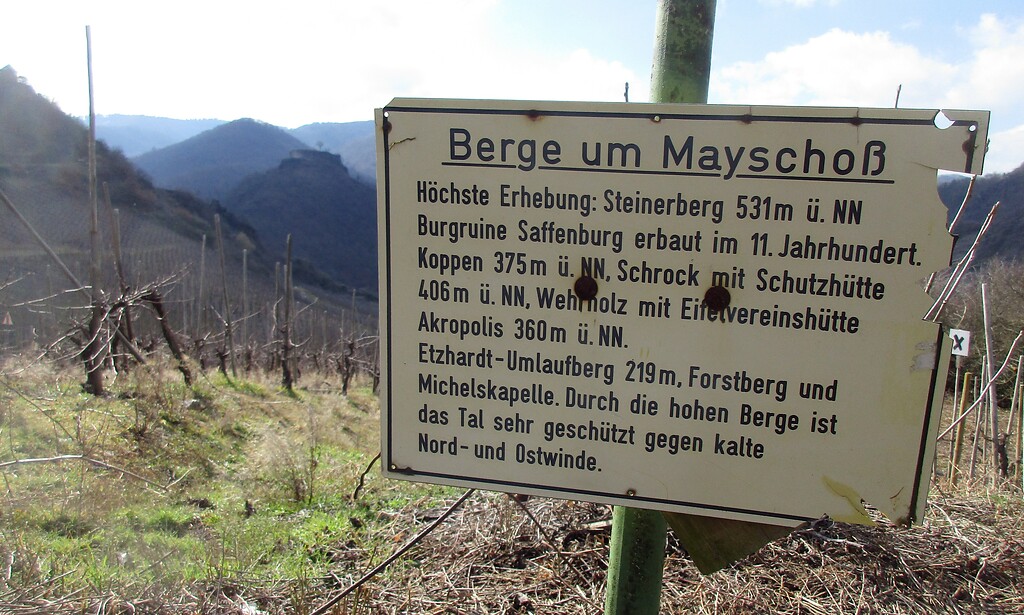 Informationstafel "Berge um Mayschoß" oberhalb des Ortes Mayschoß am Rotweinwanderweg im Ahrtal (2021). Unmittelbar links der Tafel ist im Hintergrund die Bergkuppe mit der Burgruine Saffenburg zu sehen.