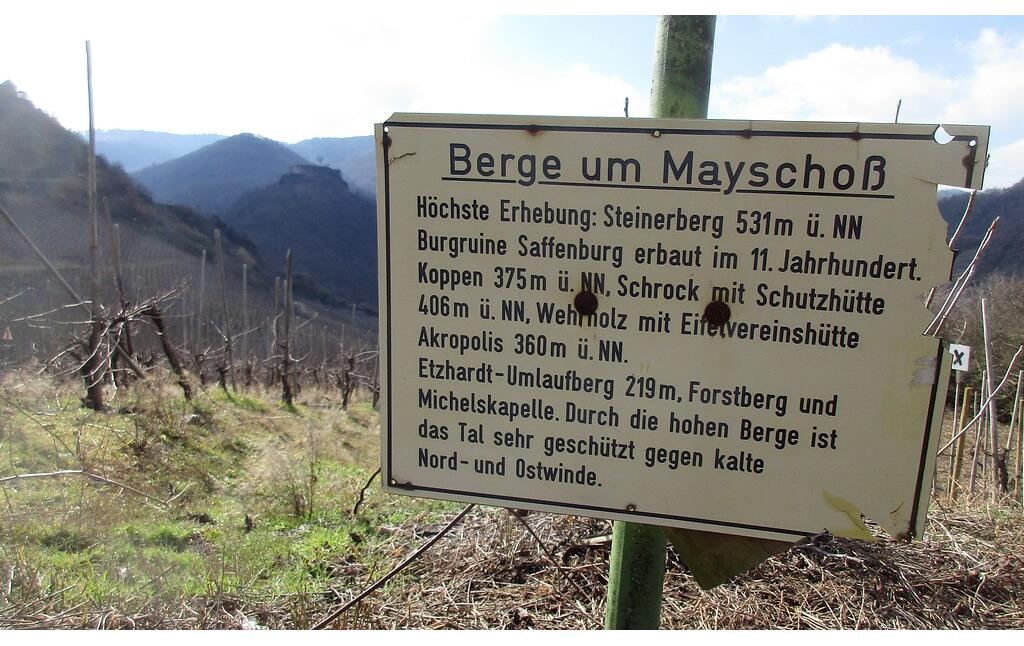 Informationstafel "Berge um Mayschoß" oberhalb des Ortes Mayschoß am Rotweinwanderweg im Ahrtal (2021). Unmittelbar links der Tafel ist im Hintergrund die Bergkuppe mit der Burgruine Saffenburg zu sehen.
