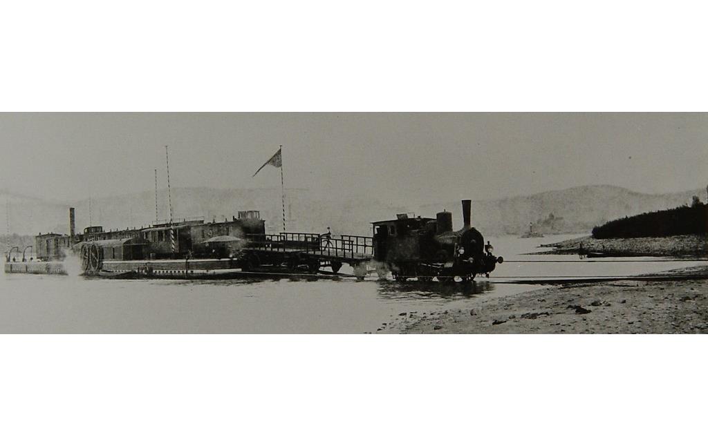 Historische Aufnahme von um 1900: Die Ponte im Fährhafen Bonn, eine Dampflokomotive zieht einen Personenzug mit sechs Wagen vom Trajekt.