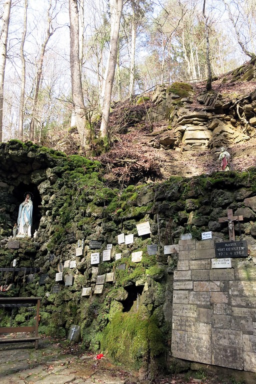 Die Mariengrotte im Albachtal bei Bitburg: links im Bild die Marienfigur in der Grotte, rechts verschiedene Dankestafeln (2015).