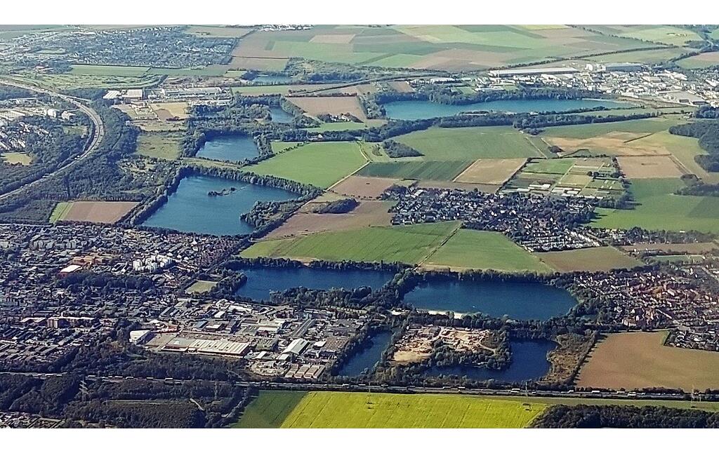 Luftbildaufnahme von Köln-Esch/Auweiler und -Pesch in westliche Blickrichtung (2021), zentral rechts im Bild das Dorf Auweiler umrahmt von den umgebenden Seen, links im Bild der Stadtteil Pesch.