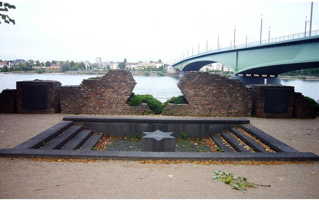 Aus Feldbacksteinen des 1938 zerstörten jüdischen Gotteshauses errichtete Gedenkstätte an die Alte Bonner Synagoge am Moses-Hess-Ufer in Bonn, dahinter die Kennedybrücke (2011).