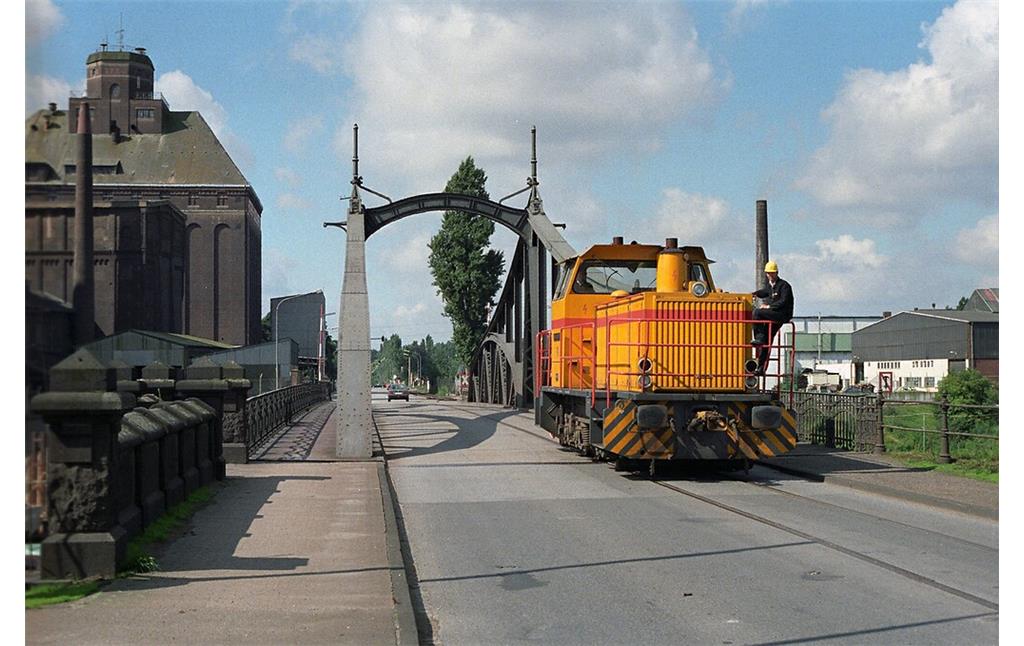 Die dieselhydraulische Güterlokomotive "Stadt Krefeld D II" des Typs Maschinenbau Kiel (MaK) G 763 C befährt die Jugendstil-Drehbrücke im Krefelder Rheinhafen über das zu diesem Zeitpunkt noch vorhandene Bahngleis (1988).