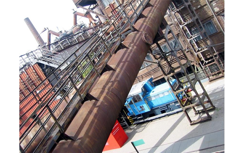 Blick über technische Anlagen der UNESCO Welterbestätte Völklinger Hütte: im Hintergrund Hochöfen, mittig eine Transportrampe und rechts unten eine Lokomotive der Werksbahn (2007).