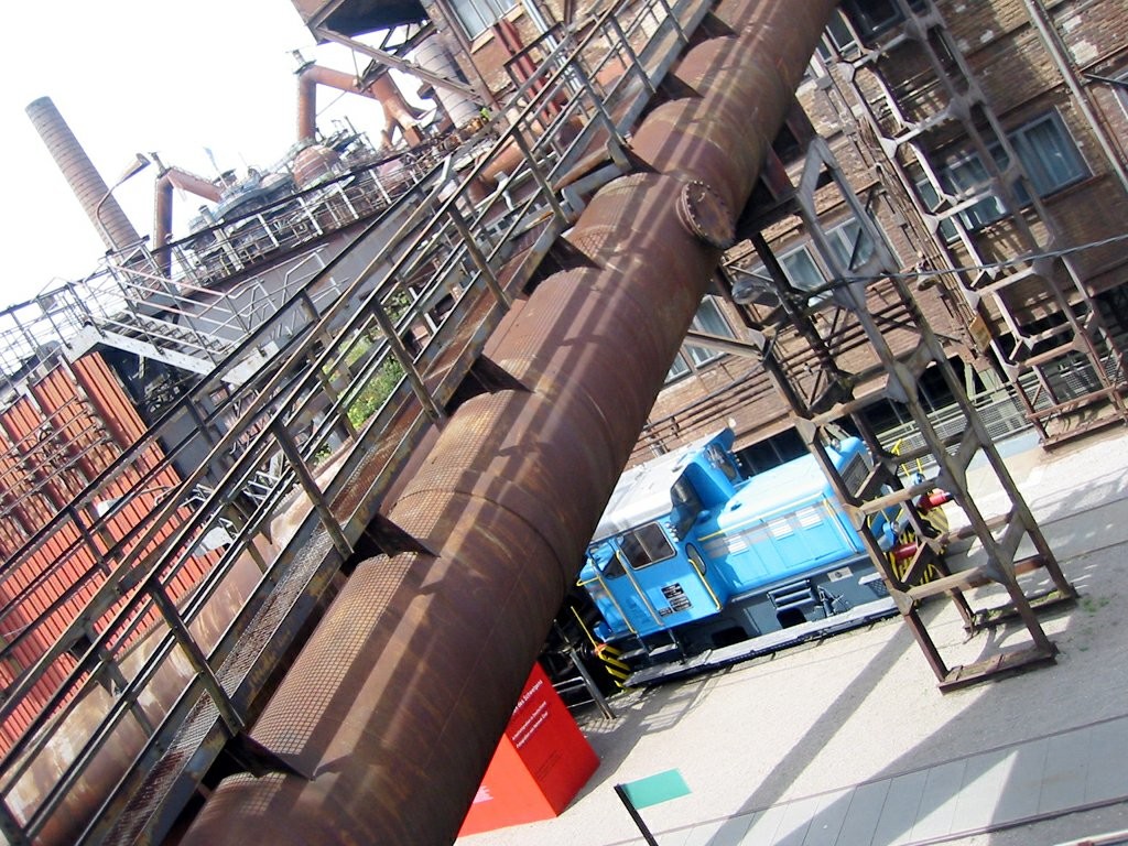 Blick über technische Anlagen der UNESCO Welterbestätte Völklinger Hütte: im Hintergrund Hochöfen, mittig eine Transportrampe und rechts unten eine Lokomotive der Werksbahn (2007).