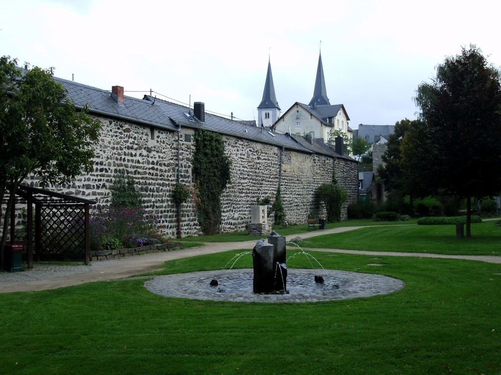 Teil der ehemaligen Stadtmauer von Montabaur. Vor der Mauer befindet sich eine kleine Parkanlage mit Brunnen (2014)