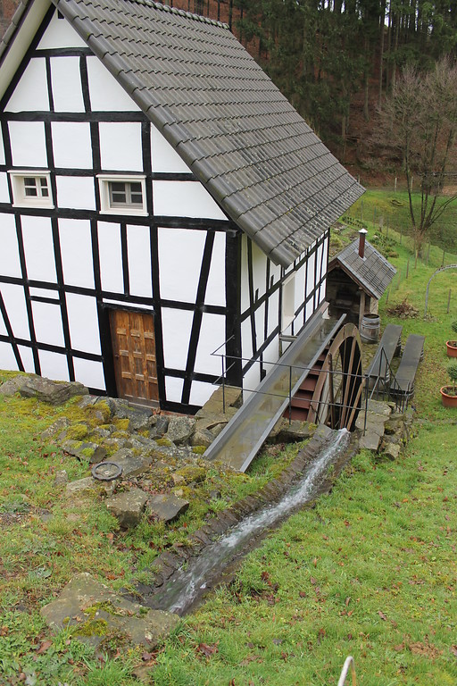 Das Mühlengebäude der Birkenmühle in Neunkirchen-Seelscheid-Birken mit Gerinne, Wasserrad und Abschlag vom Staudamm aus gesehen (2014)