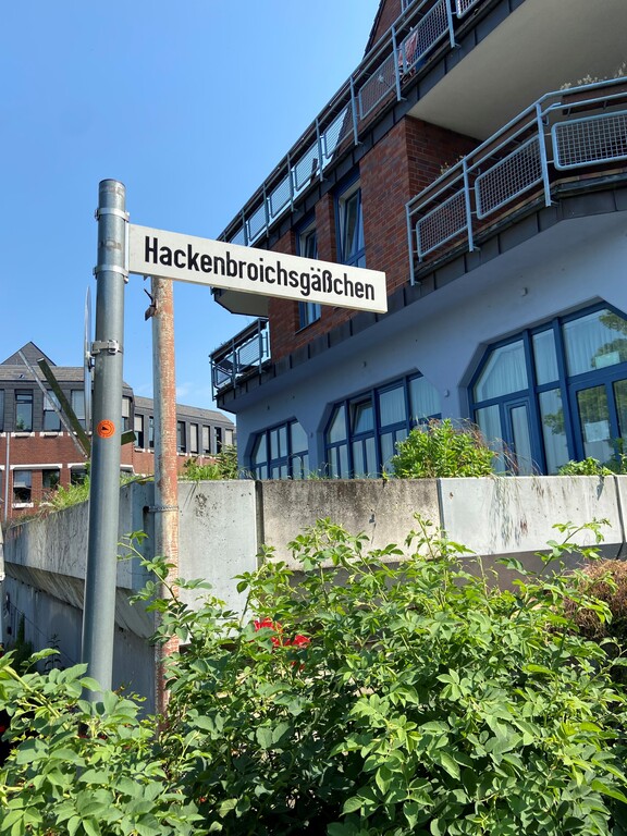 Straßenschild des Hackenbroichsgäßchen, einer kleinen Seitenstraße des Friedrich-Ebert-Ufers, in Porz (2023). Der Name erinnert an das Gasthaus "Hackenbroich", das einst hier stand.