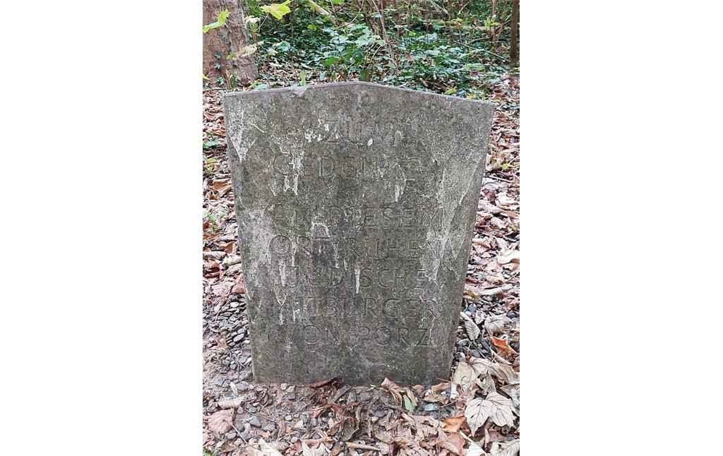 Gedenkstein am Jüdischen Friedhof am Gartenweg in Köln-Zündorf (2022). Die deutlich verwitterte Inschrift lautet: "Zum Gedenken, an diesem Ort ruhen jüdische Mitbürger von Porz".