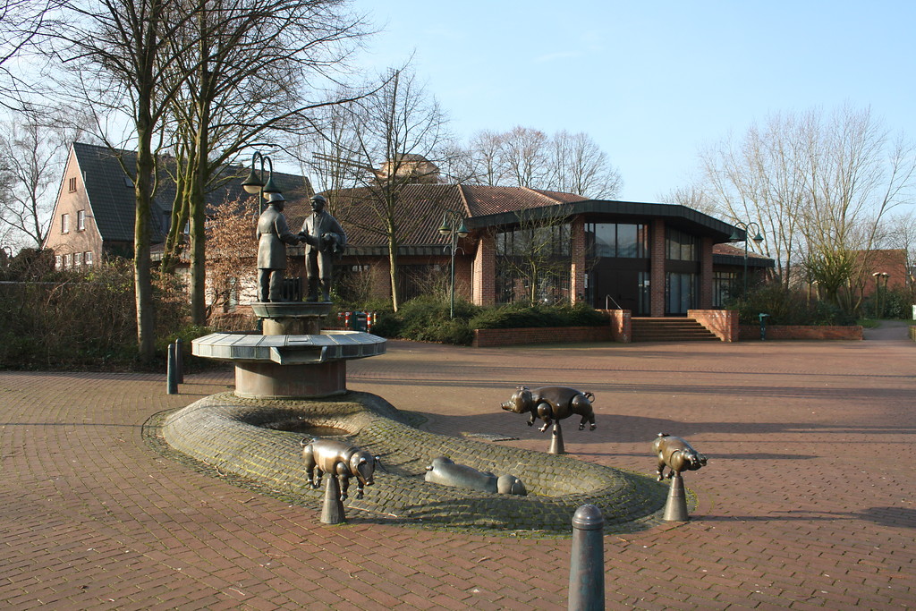 Der Ferkelbrunnen auf dem Rathausvorplatz Sonsbeck mit bronzenen Schweinen, einer Sau mit Ferkeln und zwei Handelspartnern auf der Brunnenplattform (2014)