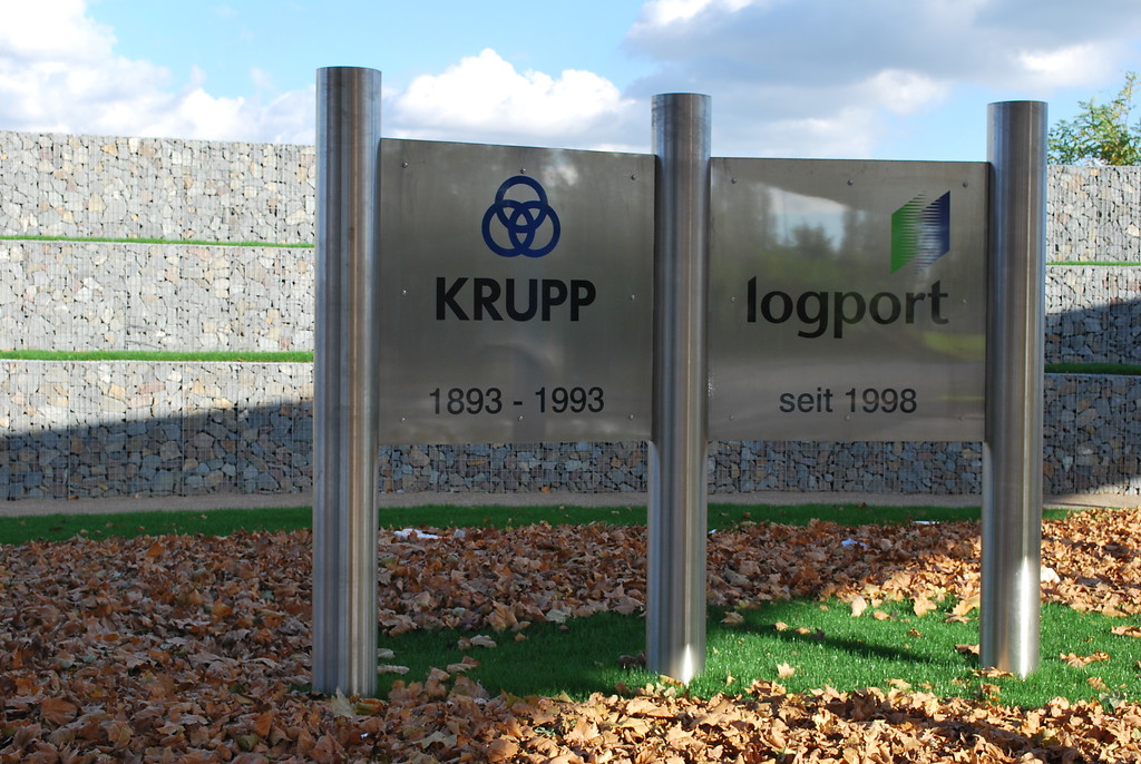 Tafel am Tor 1 des ehemaligen Krupp Stahlwerks Rheinhausen nach der Umgestaltung im Oktober 2013. Die Tafel erinnert an die ehemalige Nutzung des Geländes durch Krupp und an den Nutzungswandel zum Logistikstandort seit 1998.