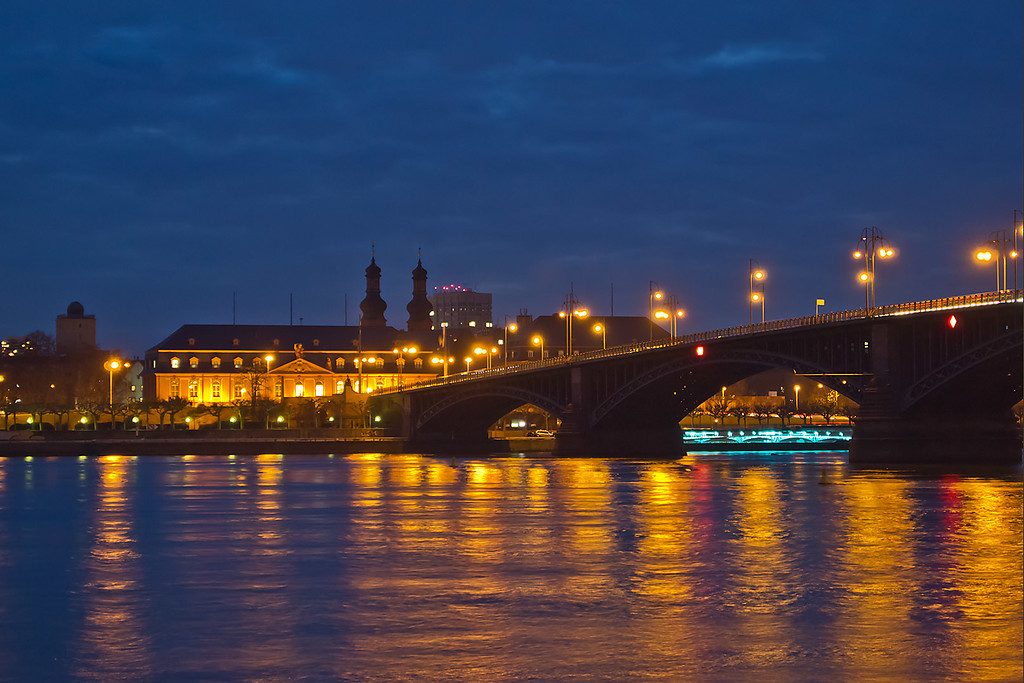 Die nächtlich beleuchtete Theodor-Heuss-Brücke über den Rhein zwischen Mainz und Wiesbaden (2013). Im Hintergrund Gebäude des Landtags Rheinland-Pfalz und die Kirchtürme von St. Peter in Mainz.
