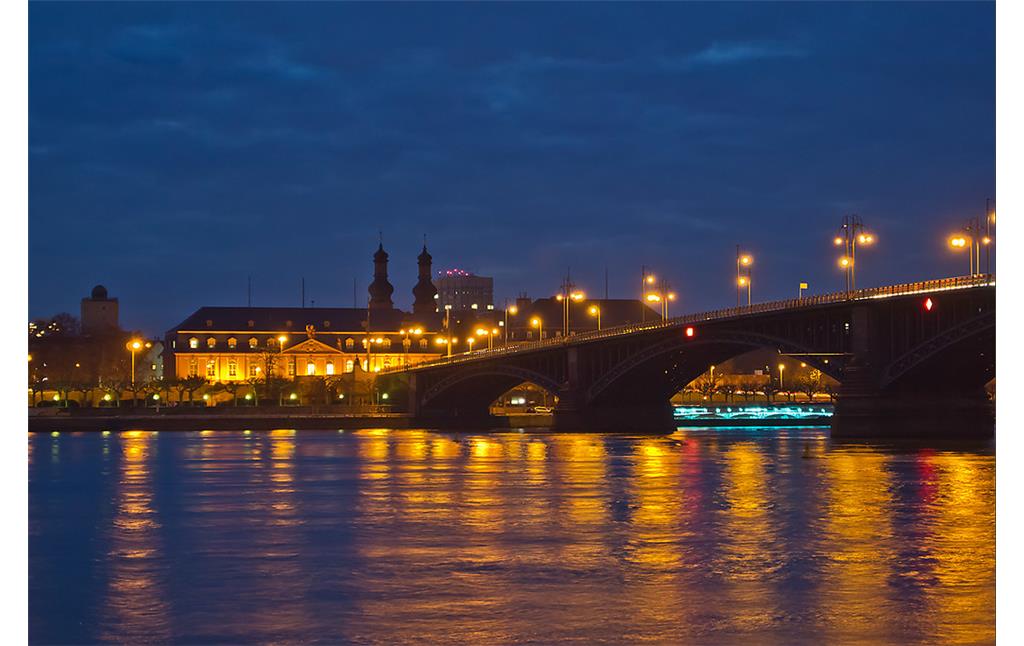 Die nächtlich beleuchtete Theodor-Heuss-Brücke über den Rhein zwischen Mainz und Wiesbaden (2013). Im Hintergrund Gebäude des Landtags Rheinland-Pfalz und die Kirchtürme von St. Peter in Mainz.