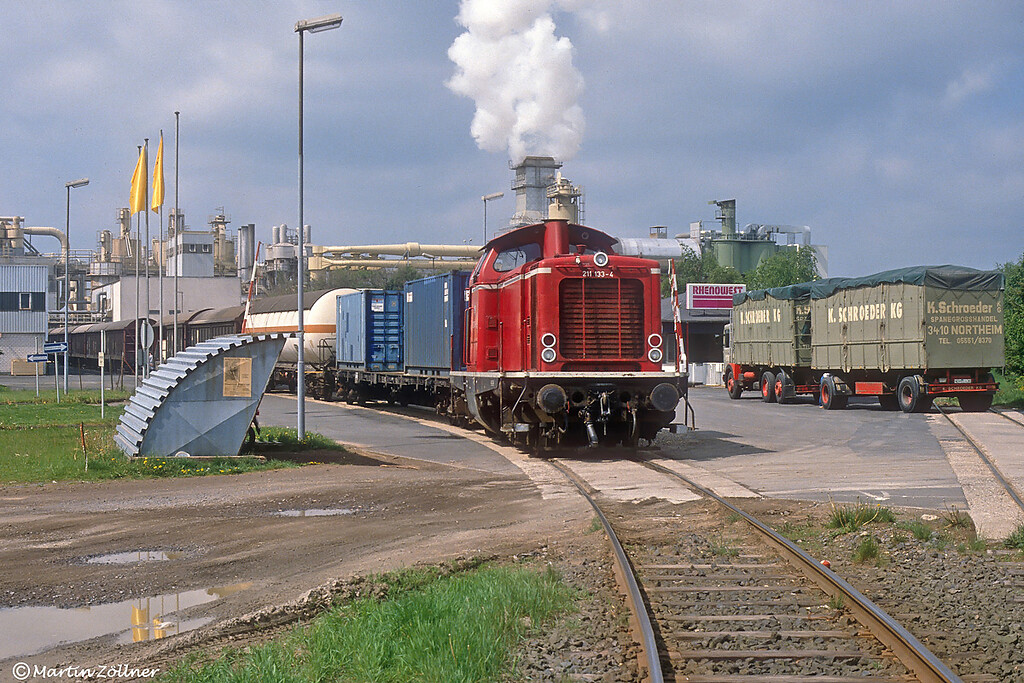 Ein Güterzug mit einer Diesellokotive des Typs der DB-Baureihe V 100 / 211 bei der Ausfahrt aus der Spanplattenfabrik Rhenowest in Kaisersesch über das dortige Industriestammgleis (1990).