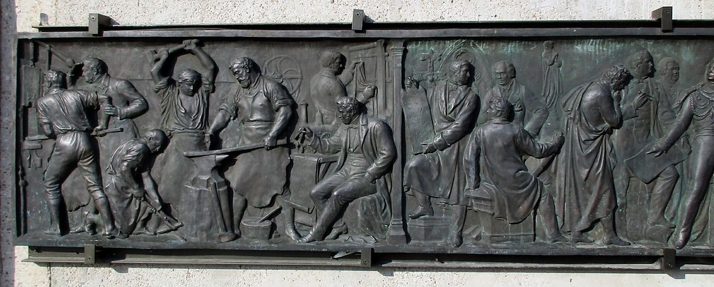Bronzene Reliefplatte auf dem Sockel des Reiterstandbilds auf dem Kölner Heumarkt: Aufschwung von Industrie und Handel (2018).