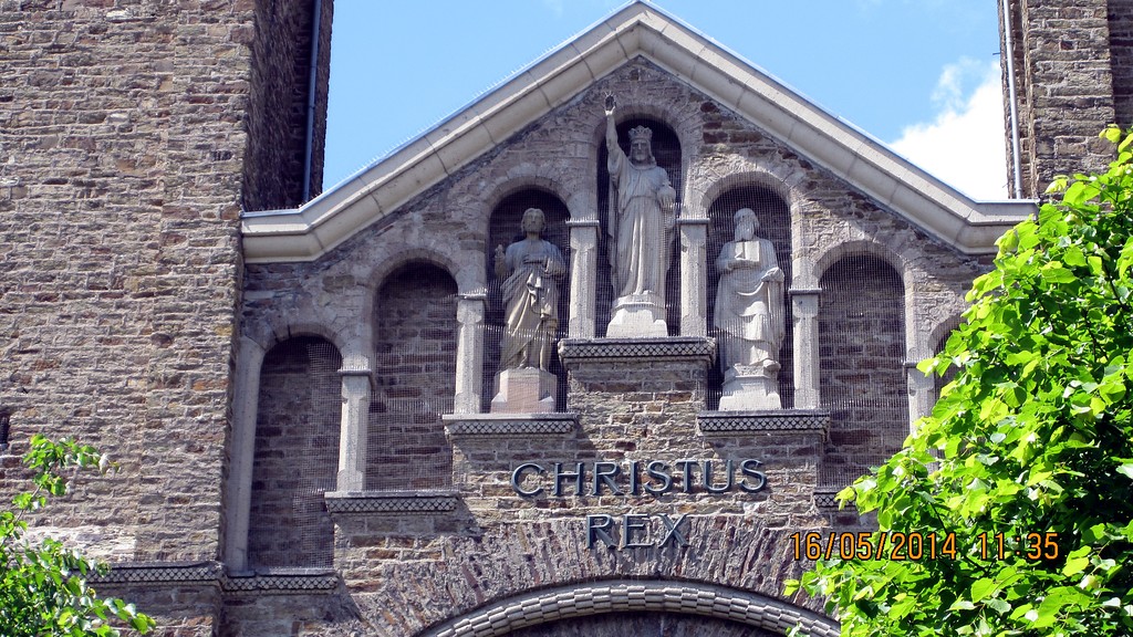 Teilansicht der neuen St. Servatiuskirche in Koblenz-Güls (2014). Zu sehen ist ein Stufengiebel, in deren drei mittleren Pfeilernischen sich Steinskulpturen befinden. In der Mitte wird Jesus Christus als König dargestellt, rechts und links von ihm befinden sich der heilige Petrus und der heilige Paulus.