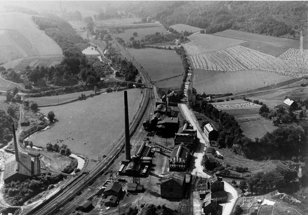 Das historische Schwarz-Weiß-Foto aus dem Jahre 1926 zeigt in der Billdmitte oberhalb des Fabrikgeländes die Hundebrücke im Deilbachtal, die über Deilbach und  Bahnlinie die Abbaugebiete mit den weiter verarbeitenden Werksgebäuden verbindet.