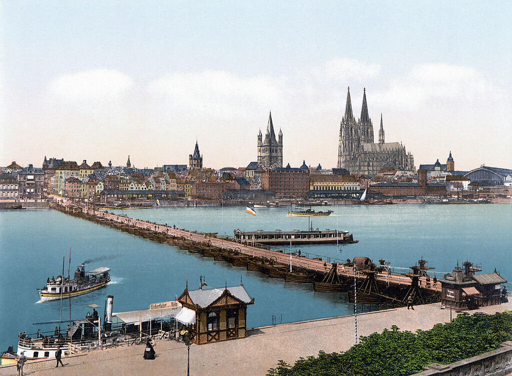 Die hölzerne Schiffsbrücke zwischen Deutz und Köln, eines der Vorgängerbauwerke der heutigen Deutzer Brücke (kolorierte Postkarte von um 1900). Im Bildvordergrund Personenfähren und mittig das an der Brücke angelegte "Badeschiff" der Flussbadeanstalt.