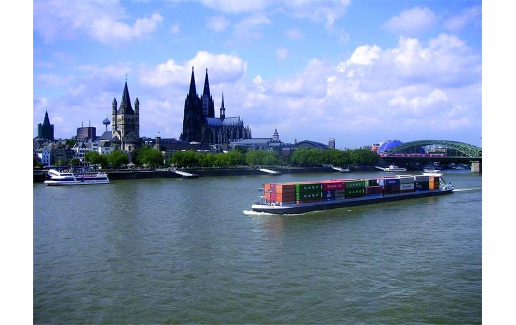 Blick auf den Rhein und die Kölner Altstadt mit dem Kölner Dom und der Hohenzollernbrücke. Im Vordergrund fährt ein voll beladenes Containerschiff flussaufwärts (2004)