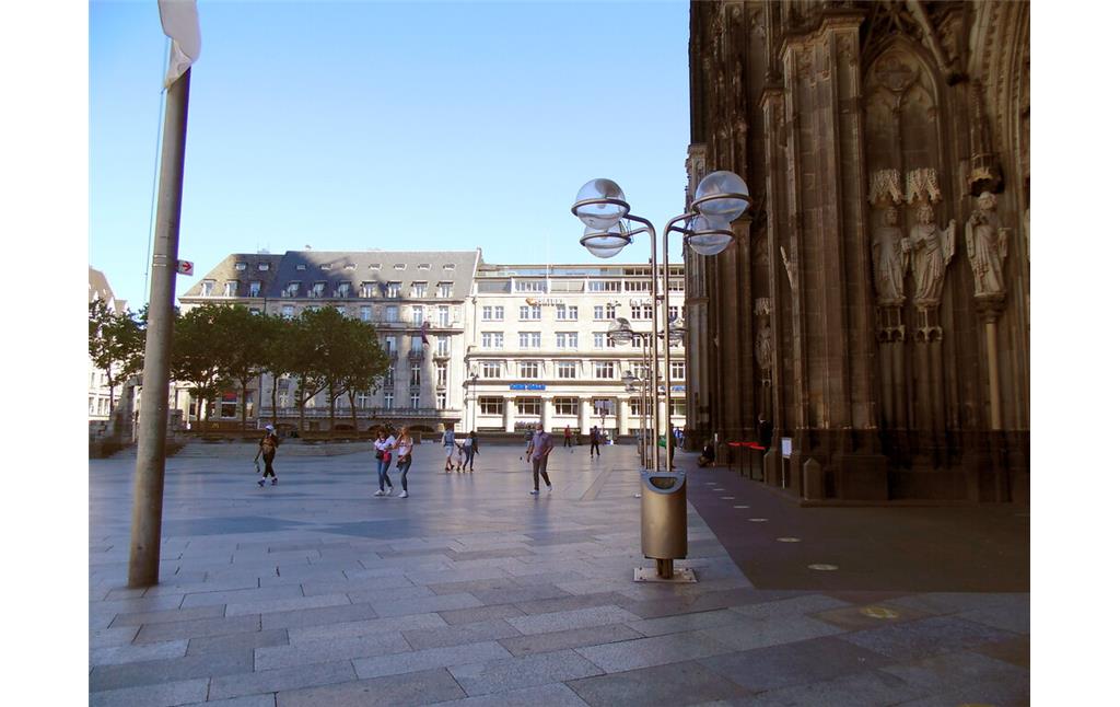 Blick von der Domplatte im Bereich der Hauptportalzone auf das im Hintergrund gelegene Deichmannhaus in der Kölner Altstadt-Nord. Links vom Deichmannhaus befindet sich das traditionsreiche Excelsior Hotel Ernst (2020).