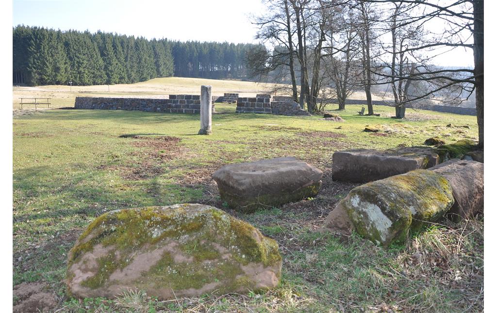 Blick auf das römische Kleinkastell in Nettersheim. Im Vordergrund lose liegende, vor Ort gefundene Bausteine und eine wieder aufgerichtete Säule (2014)