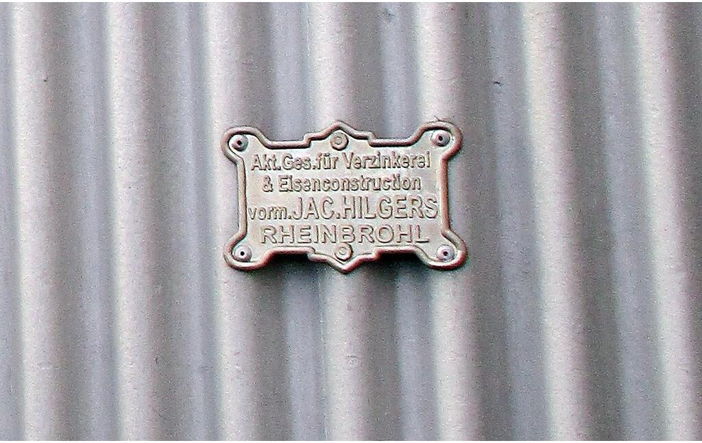 Metalltafeln an den Boxengaragen im historischen Fahrerlager am Nürburgring weisen auf die am Bau des Fahrerlagers beteiligte Firma "Akt. Ges. für Verzinkerei & Eisenkonstruktion vorm. JAC. HILGERS RHEINBROHL" hin (2020).