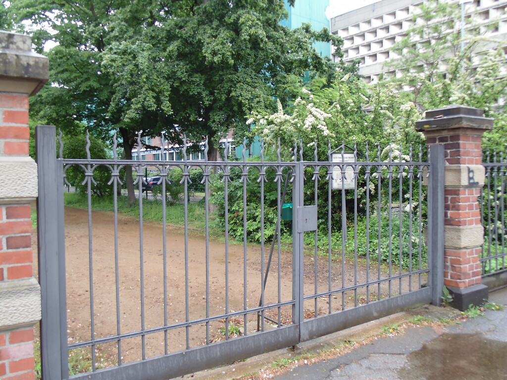 Tor des evangelischen Geusenfriedhofs in Köln-Lindenthal. Im Hintergrund ist die Fassade der Universitätsbibliothek zu sehen (2021).
