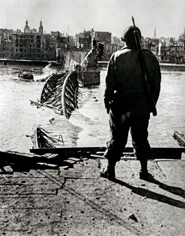 Aufnahme aus den letzten Tagen des Zweiten Weltkriegs in Bonn 1945: ein alliierter Soldat vor der am 8. März 1945 gesprengten Alten Rheinbrücke, im Hintergrund ist links die Bonner Namen-Jesu-Kirche zu erkennen.
