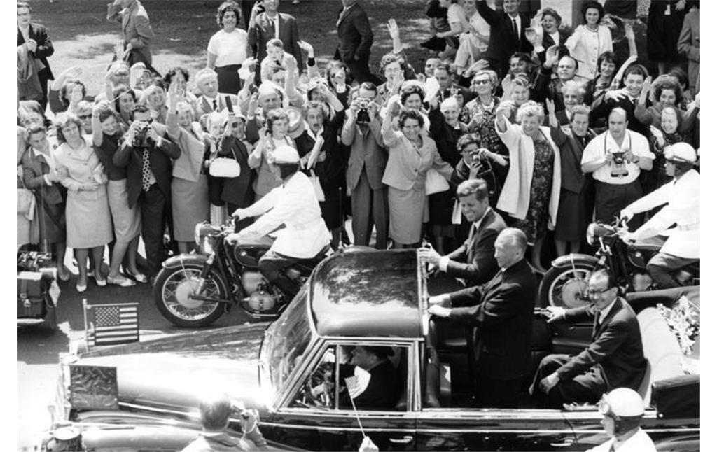 Bundeskanzler Konrad Adenauer und US-Präsident John F. Kennedy während des Staatsbesuchs 1963 bei der Fahrt im offenen Wagen durch ein Spalier jubelnder Zuschauer (23. Juni 1963)