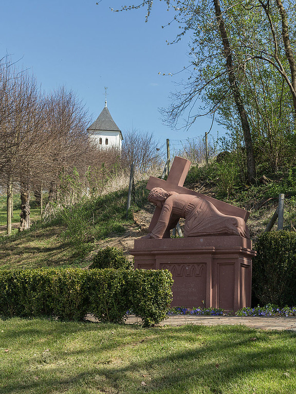 Blick auf eine Skulptur mit Jesus unter dem Kreuz in Weilerswist, im Hintergrund das Swister Türmchen (2015).