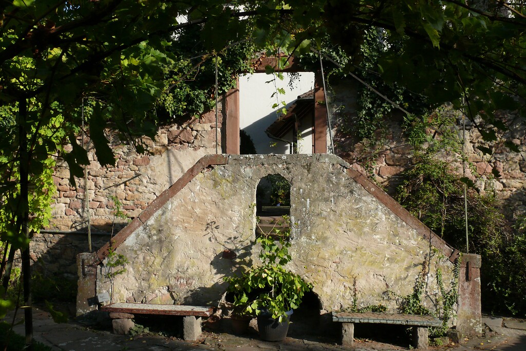 Hinter dem Pfarrhaus in Kirrweiler befindet sich ein Hof. Von dort aus hat man durch eine Mauer Zugang zum Pfarrgarten (2021)