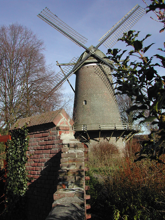 Die Gommansche Mühle in Sonsbeck mit den unbespannten Flügeln vor der nachempfundenen Stadtmauer, einer lückigen Ziegelmauer.