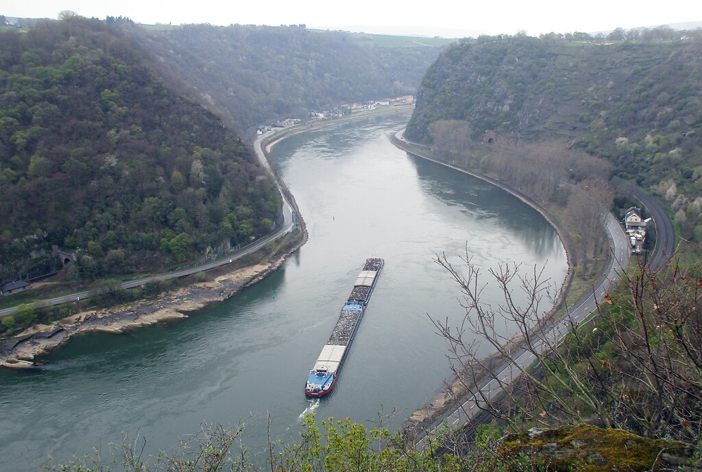 Das Rheintal vor Sankt Goarshausen: Ein Schubverband steuert auf die enge Flusskurve am Loreleyfelsen zu, rechts im Bild die Bahnstrecke mit den Loreley-Tunneln (2021).