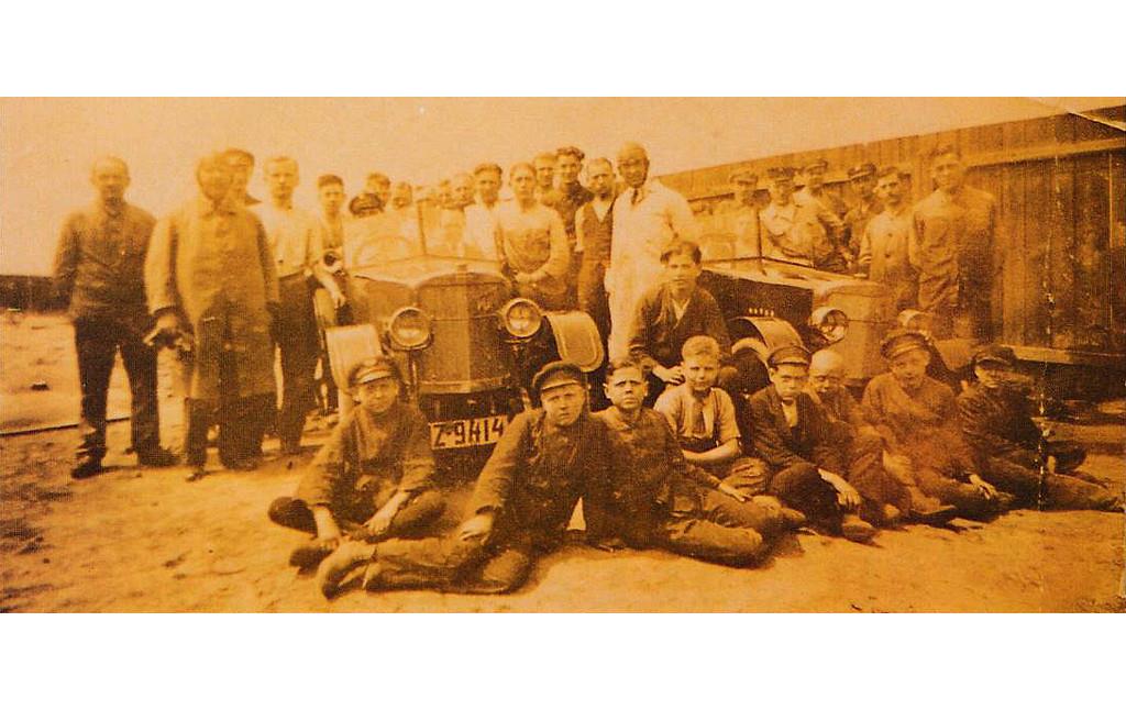 Historische Aufnahme (zwischen 1921 und 1924): Die 31 Personen umfassende Belegschaft der "Fox Automobilwerke AG" in Köln-Dellbrück vor zwei fertiggestellten Fahrzeugen.