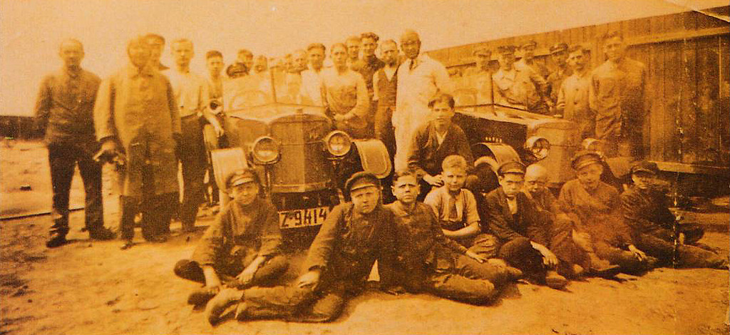 Historische Aufnahme (zwischen 1921 und 1924): Die 31 Personen umfassende Belegschaft der "Fox Automobilwerke AG" in Köln-Dellbrück vor zwei fertiggestellten Fahrzeugen.