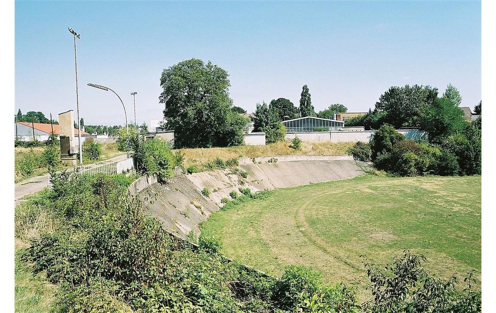 Das im Verfall begriffene Bonner Poststadion mit den umlaufenden Steilkurven der Radrennbahn (2005), links die Gedenkstele für Ferdinand August Schmidt