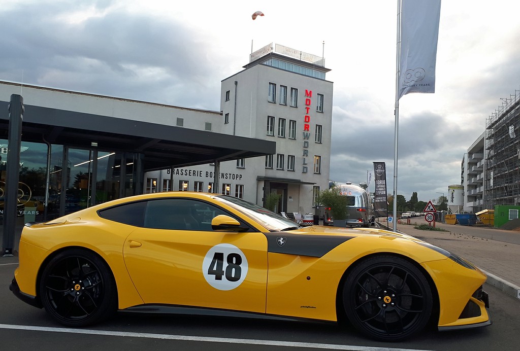 Der Tower des ehemaligen Flughafens Butzweilerhof in Köln-Ossendorf, heute genutzt als Teil der "Motorworld Köln" (2019), im Bildvordergrund ein Ferrari-Sportwagen.