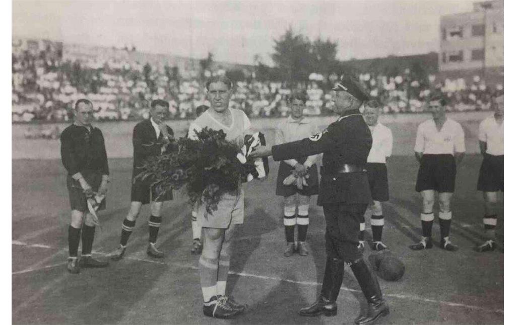 Ein Offizieller in NS-Uniform begrüßt den Mannschaftskapitän des FC Schalke 04, Ernst Kuzorra (1905-1990), vor dem Fußballspiel zwischen der Mannschaft der TuRa Bonn und dem FC Schalke 04.